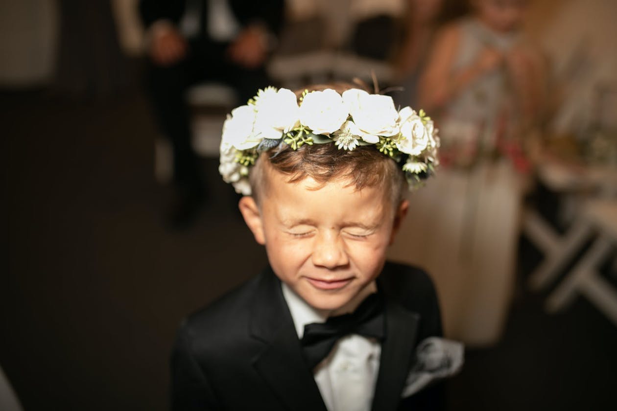 Little boy closes his eyes while wearing white flower crown | PartySlate