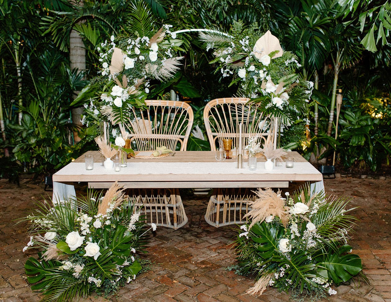 Sweetheart table with rattan seating and monstera leaf décor | PartySlate