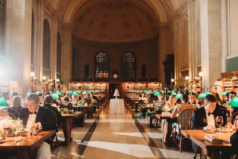 Boston wedding at the Boston public Library with guests seated at library tables with green glass lanterns at each table | PartySlate