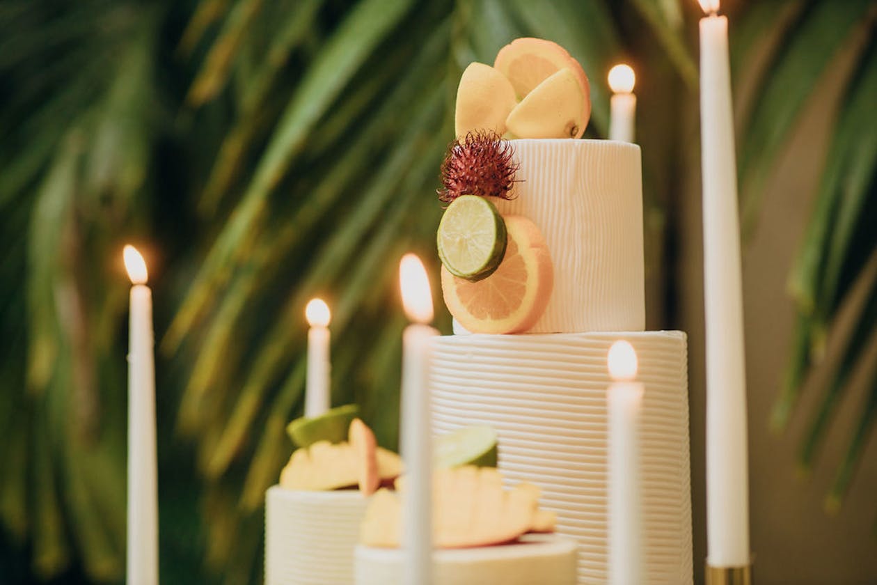 White wedding cake with fruit décor surrounded by white tapered candles | PartySlate