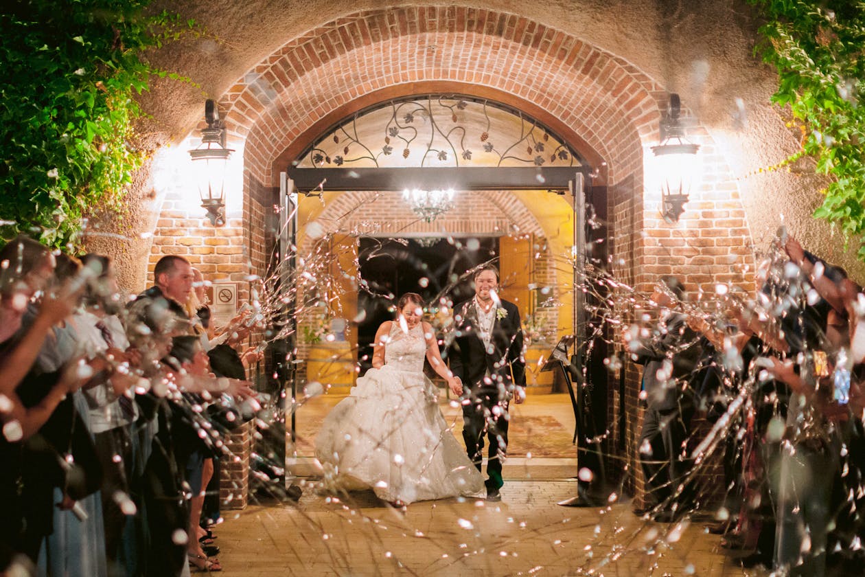 Couple exiting wedding venue at night while guests stand on either side of them throwing streamers in celebration | PartySlate