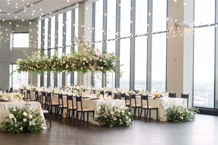 Mezzanine grand room at wedding venue in boston with tall greenery centerpieces on tables and on the floor with twinkle lights hanging from ceiling | PartySlate
