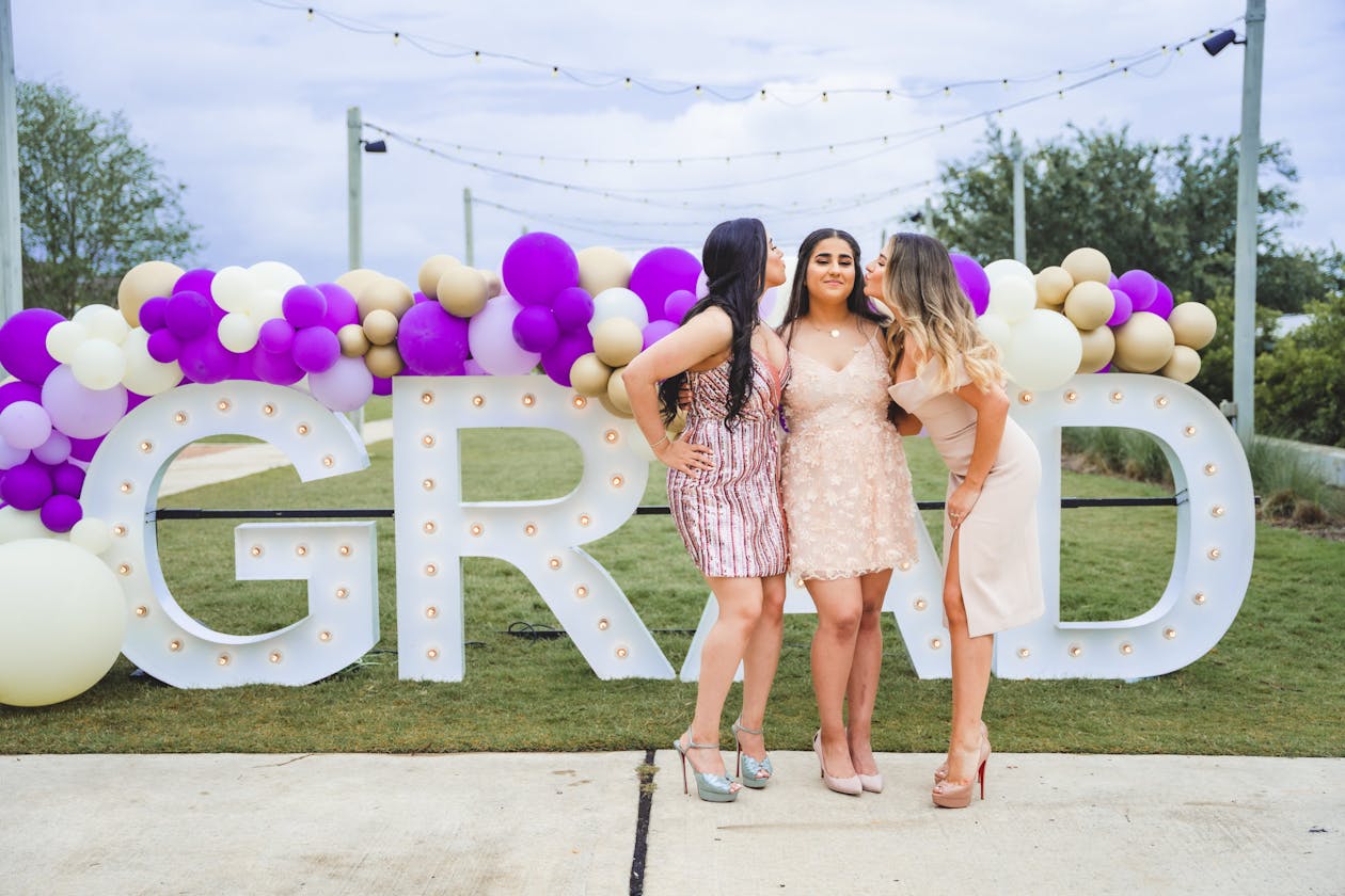 balloons on a marquee sign that says grad with three girls posing in front of it | PartySlate