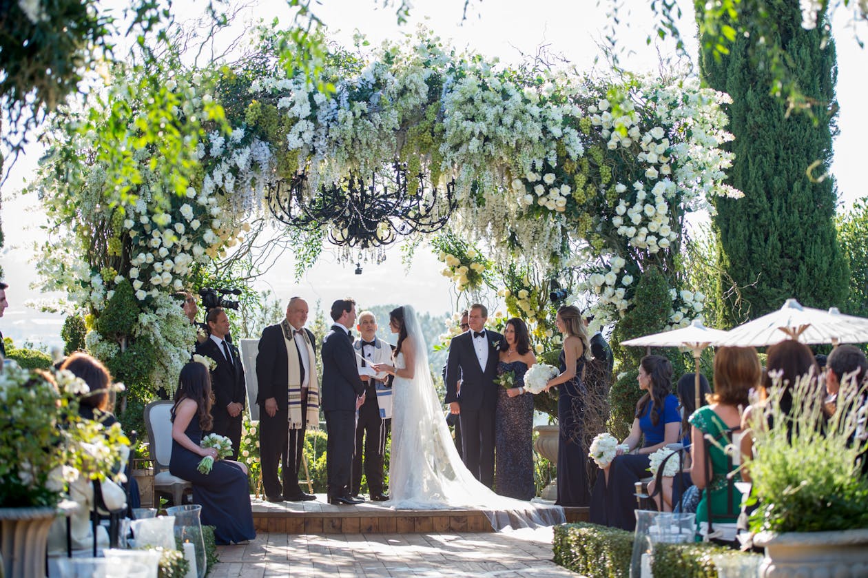 Jewish wedding under lush white and green floral chuppah with chandelier | PartySlate
