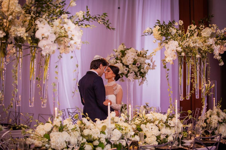 Glamorous boston wedding with white florals surrounding couple looking at each other dressed in wedding dress and tux | PartySlate