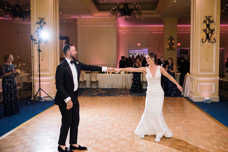 Couple dancing at their boston wedding reception with guests standing in the back of the room watching | PartySlate