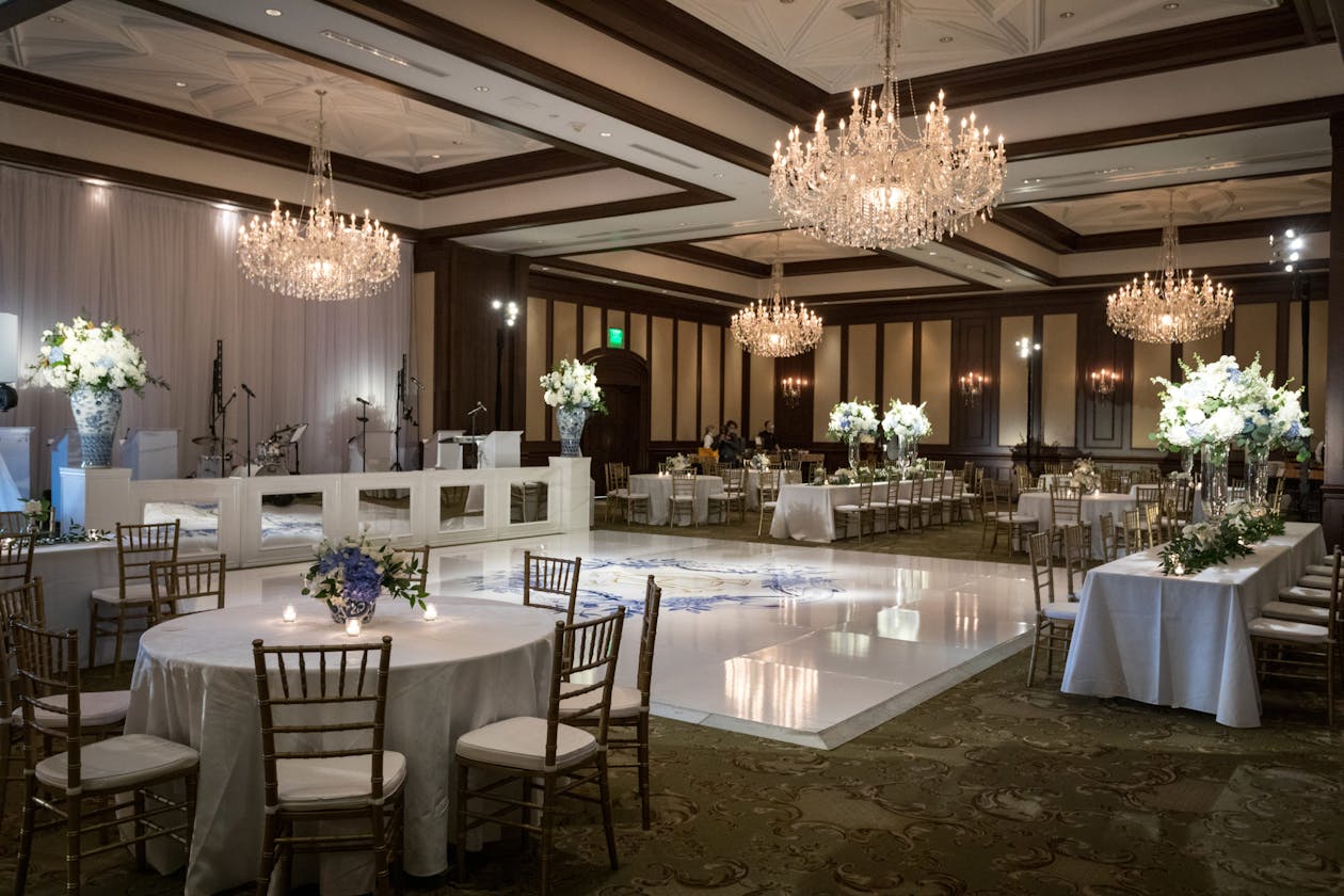 Reception venue with white dance floor and round tables surrounding it | PartySlate