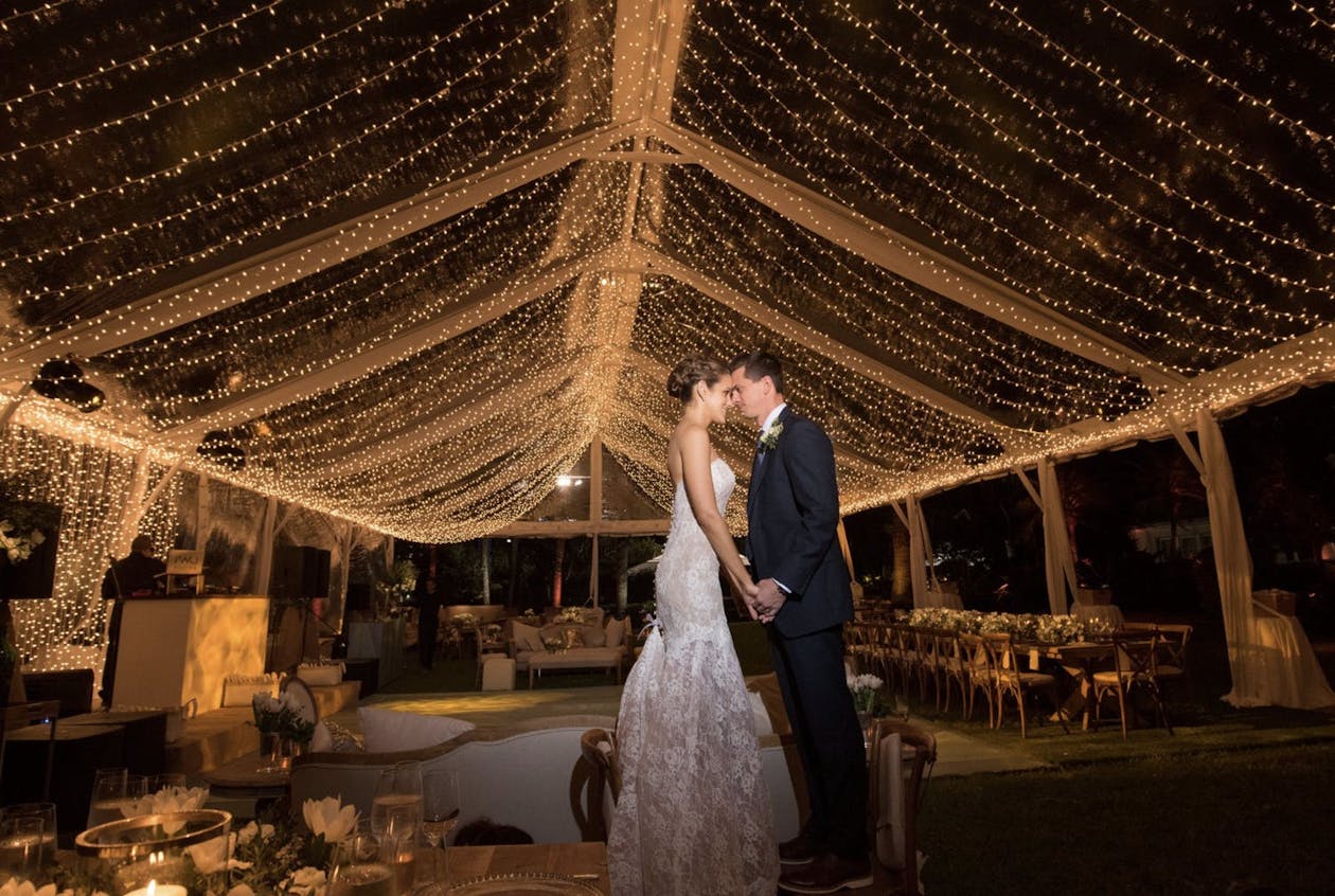 Couple dances beneath string light wedding tent | PartySlate