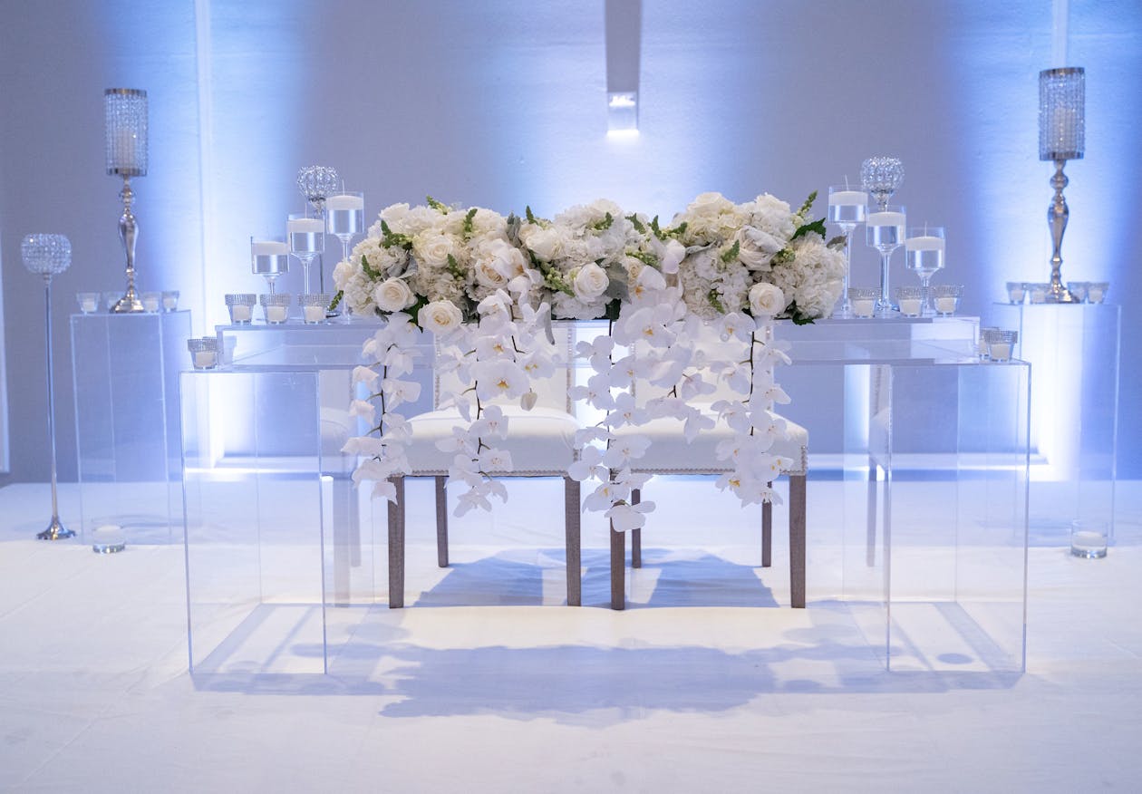 Lucite sweetheart table with white florals on top and cool lighting behind | PartySlate