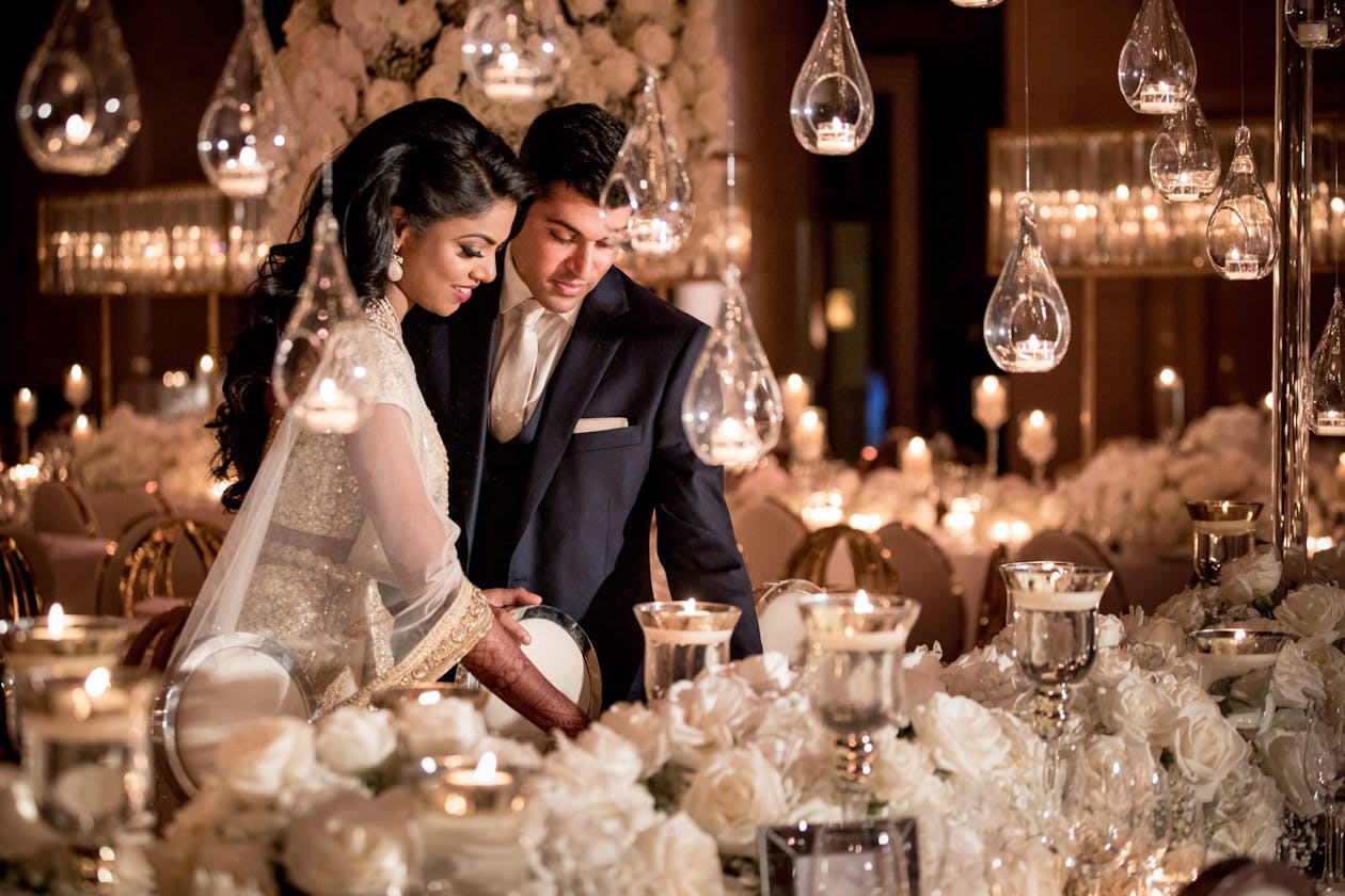 Couple looks at lavish tablescape with suspended globed candle light at South Asian fairytale wedding | PartySlate