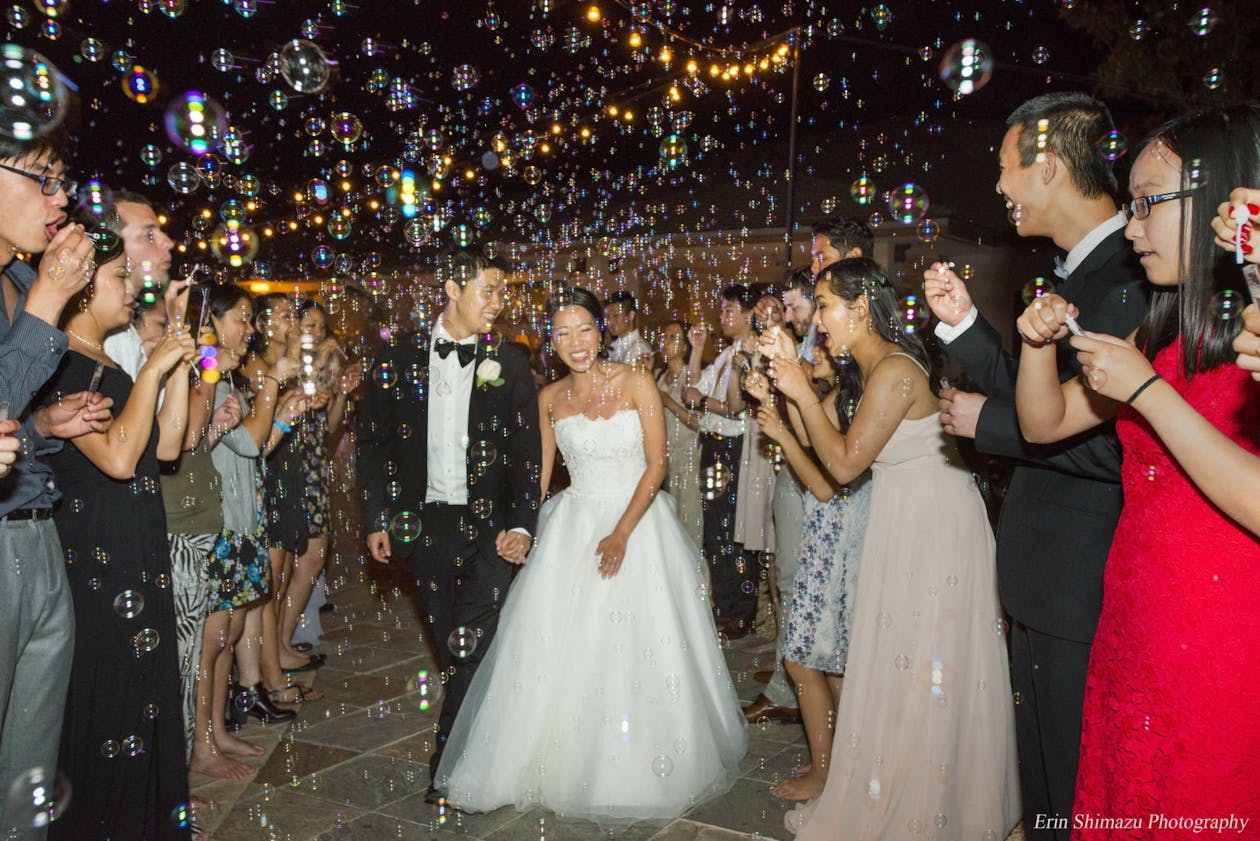 wedding exit with bubbles floating around couple while they leave their reception venue | PartySlate