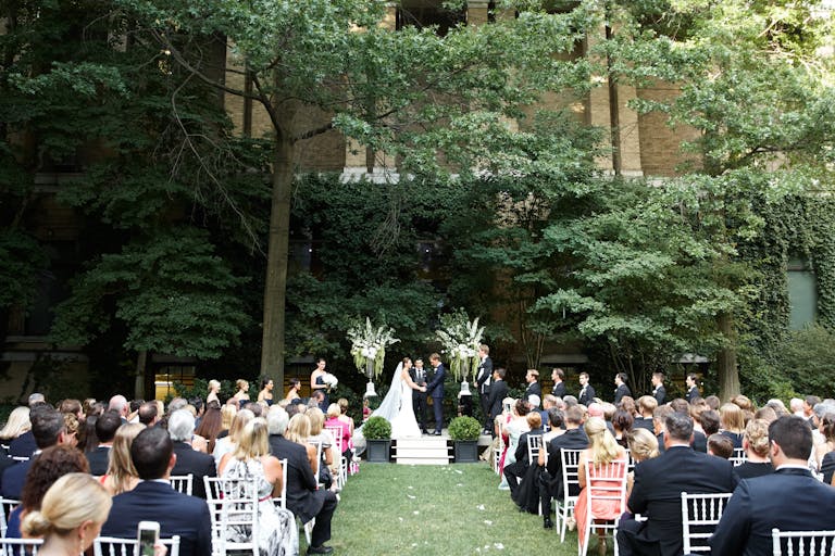 Wedding ceremony at the Museum of Fine Arts in Boston outside with natural greenery all around and guests seated in front of alter | PartySlate