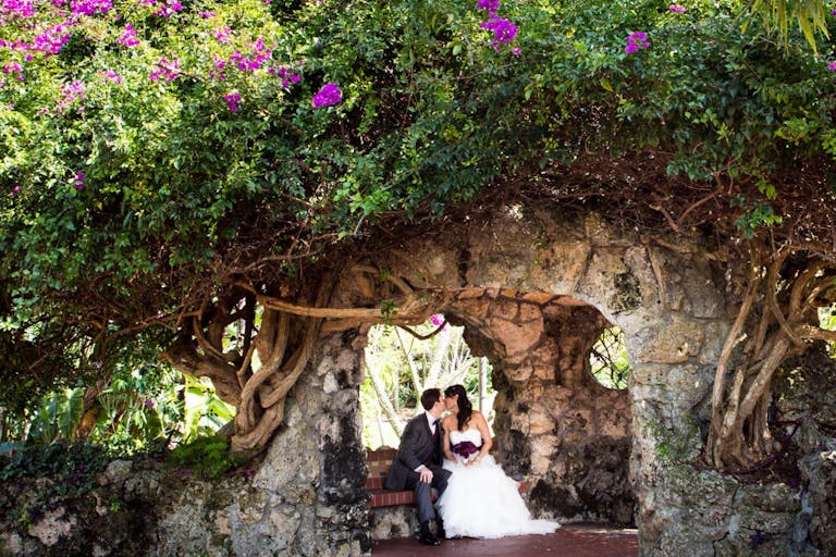 wedding at Pinecrest Gardens in miami with couple sitting in garden inside rock cave | PartySlate