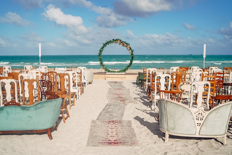 eclectic beach wedding with wedding aisle lined with different style seating and arch at the end | PartySlate