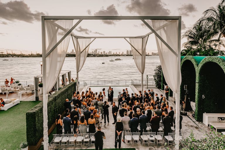 all white outdoor wedding at Mondrian South Beach with couple standing at the alter in front of the ocean with guests around | PartySlate