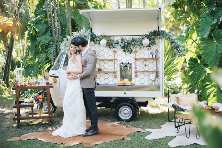 married couple posing in front of outdoor vintage mobile bar | PartySlate