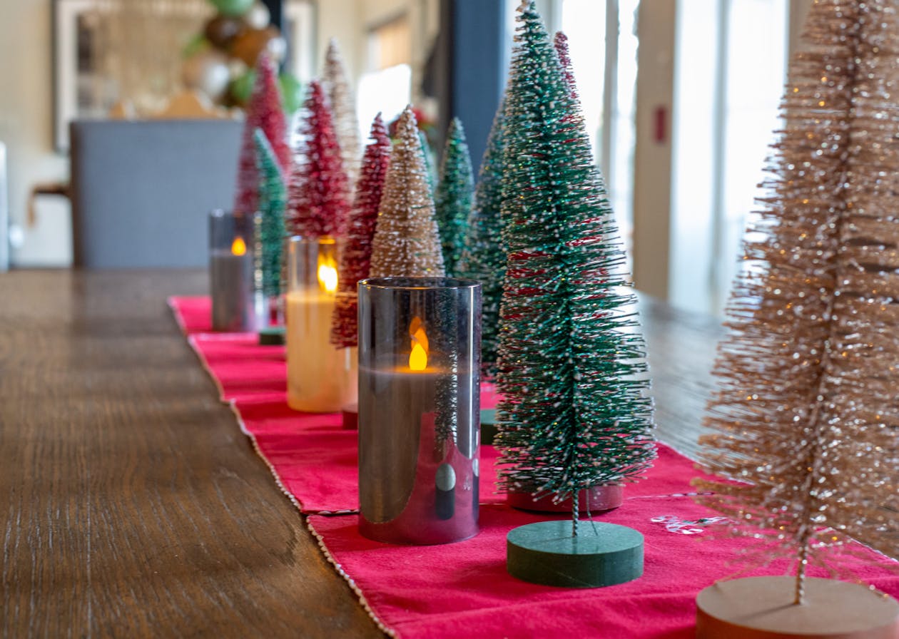 Wooden table with crimson table runner and evergreen centerpieces | PartySlate
