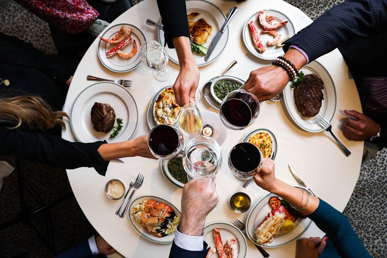 Joe’s Seafood, Prime Steak & Stone Crab areial photo of people eating dinner around a round table and making a toast with red wine | PartySlate
