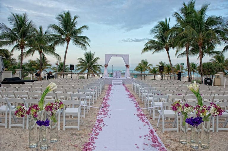 tropical wedding aisle on the beach with rose petals lining it | PartySlate