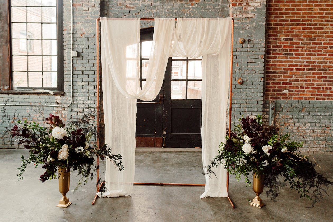 Modern industrial wedding arch with white drapery | PartySlate