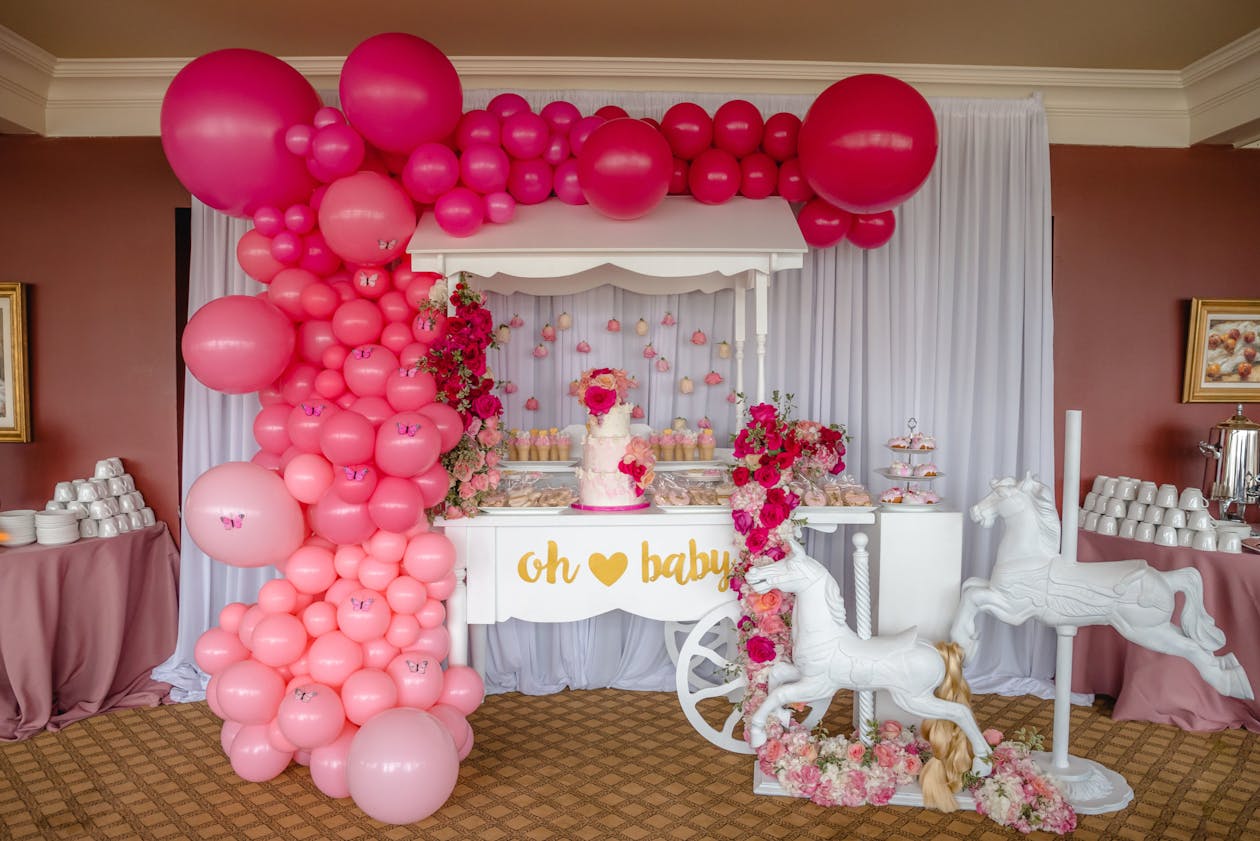 pink baby shower with balloons and decor surrounding dessert table | PartySlate