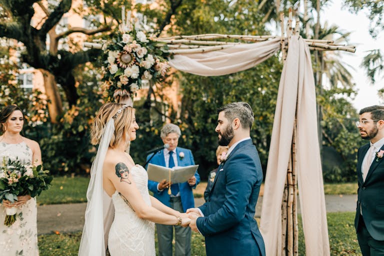 The Woman’s Club of Coconut Grove outdoor wedding venues miami couple getting married in front of officiant and wedding arch | PartySlate