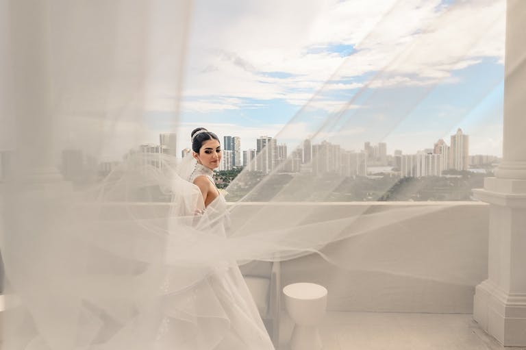 bride standing outside with her vail blowing in the wind | PartySlate