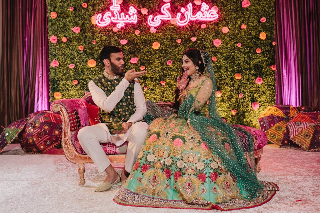 Couple in green traditional attire at sangeet with boxwood backdrop and neon signage | PartySlate