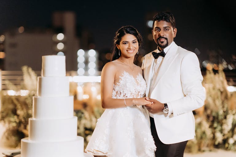 fairytale wedding at Event Space at 1111 Lincoln Road in Miami with couple standing by all white wedding cake | PartySlate