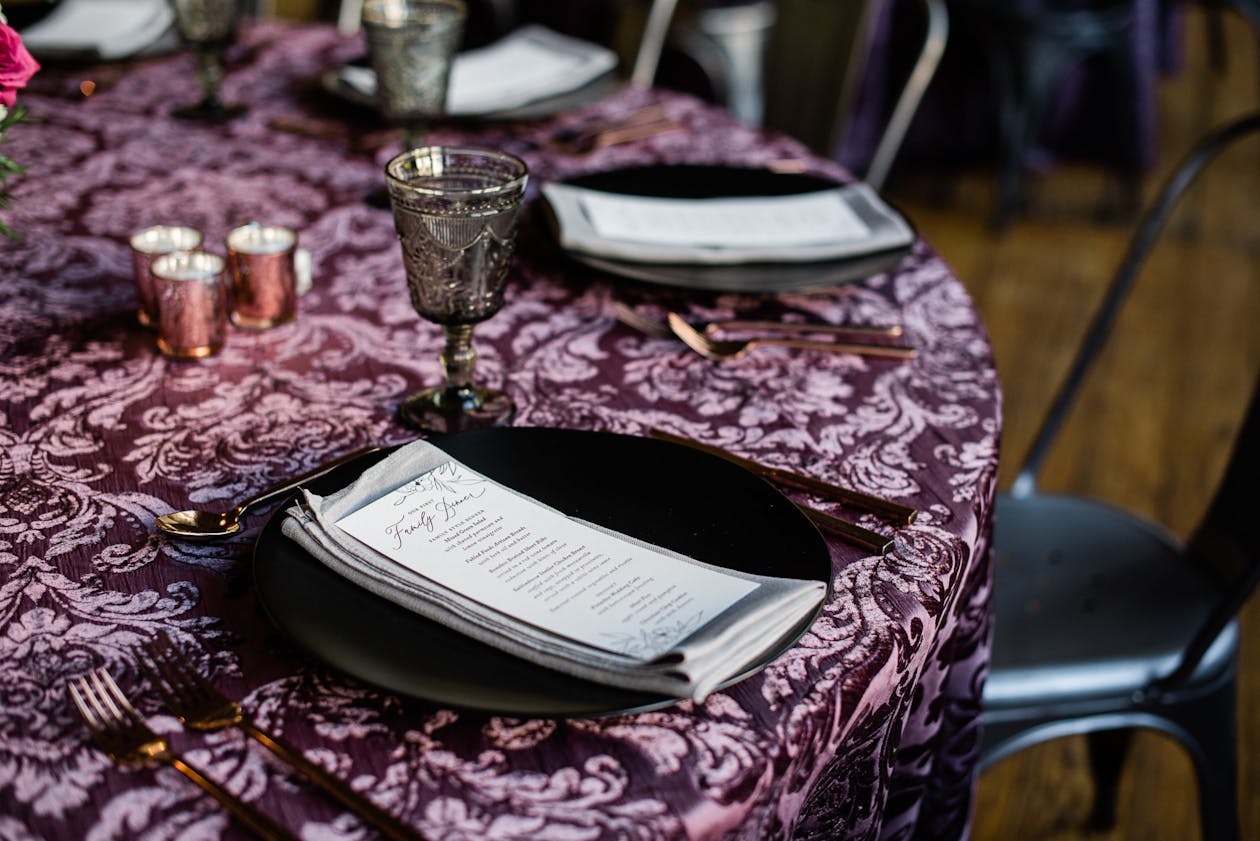 Wedding reception table with purple linen and black tableware | PartySlate