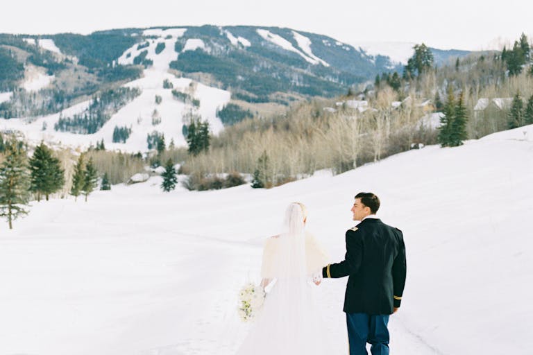 winter wonderland wedding with couple walking through snow outside with mountains in the back | PartySlate