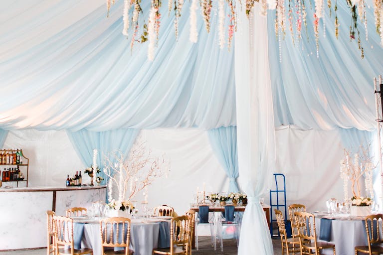 indoor tented wedding with blue and white accents and colorful florals hanging from the ceiling | PartySlate