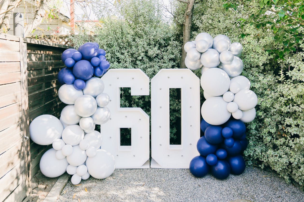 60th birthday party signage with white and blue balloons around | PartySlate