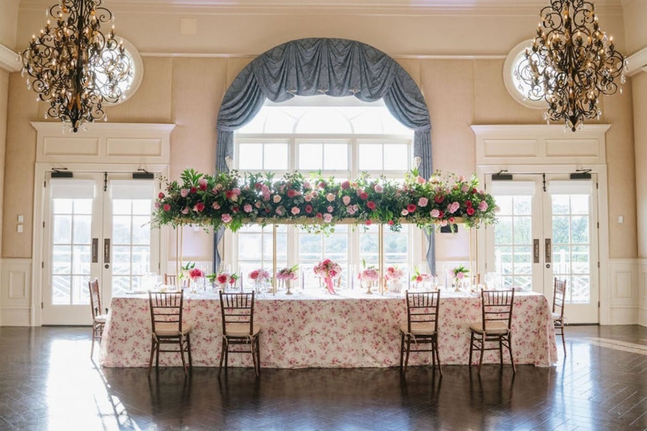 Kings table with pink floral linen and elevated greenery | PartySlate