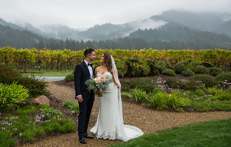 couple standing outside in front of vineyard on their wedding day | PartySlate