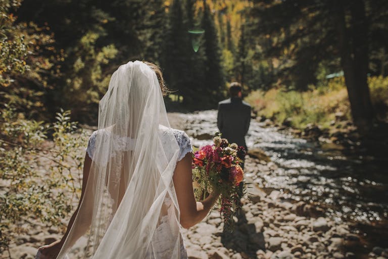 Sonnenalp Hotel colorado mountain wedding venue with couple walking away from camera and bride holding bouquet of colorful flowers | PartySlate