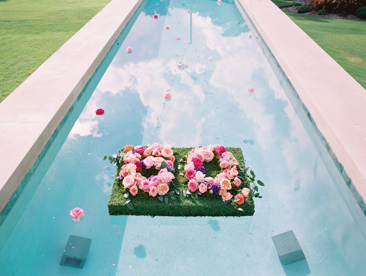 colorful floral 60th birthday party idea with floral signage floating in backyard pool | PartySlate