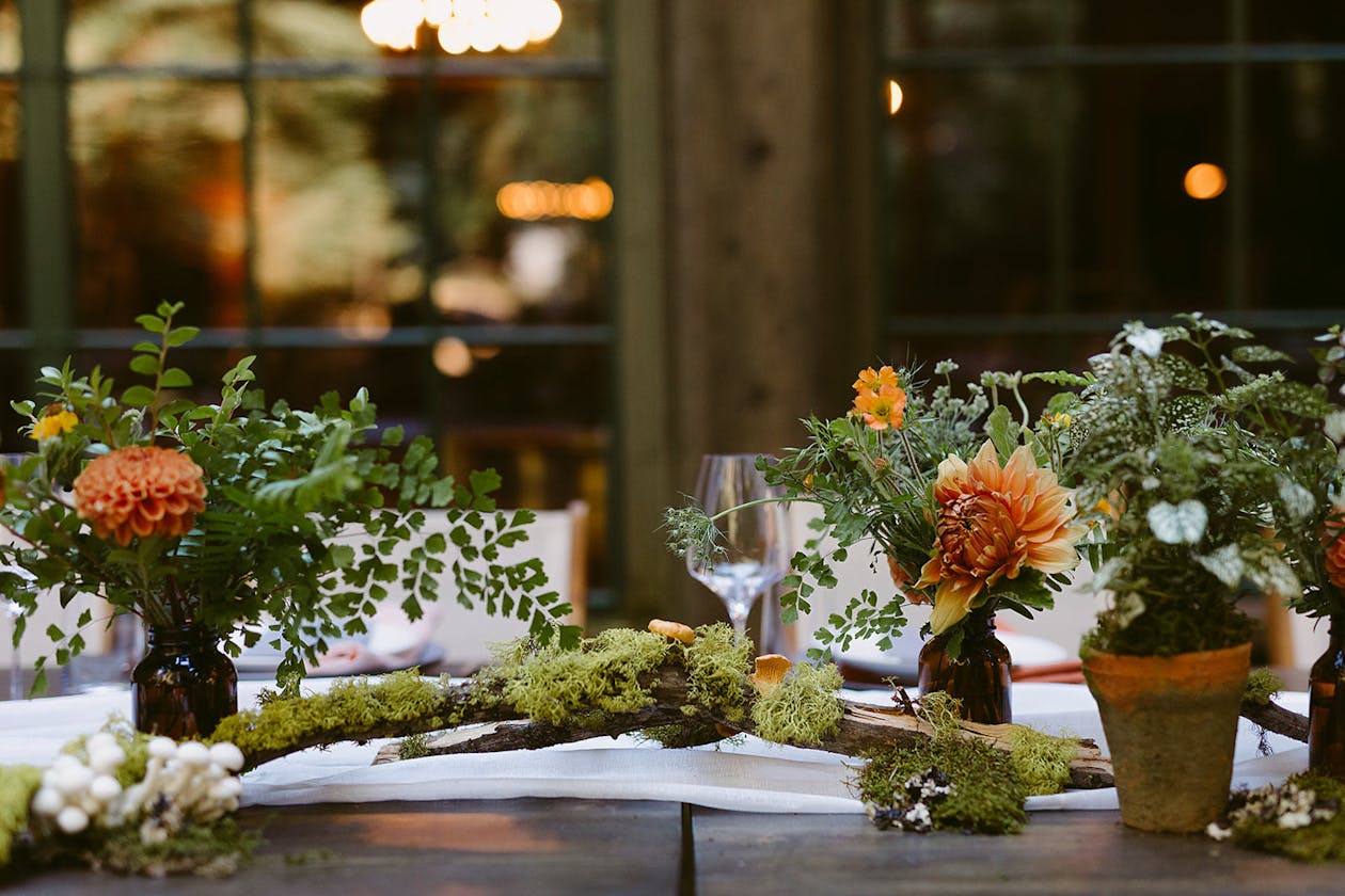 Wedding centerpieces with driftwood, moss, and orange blooms | PartySlate