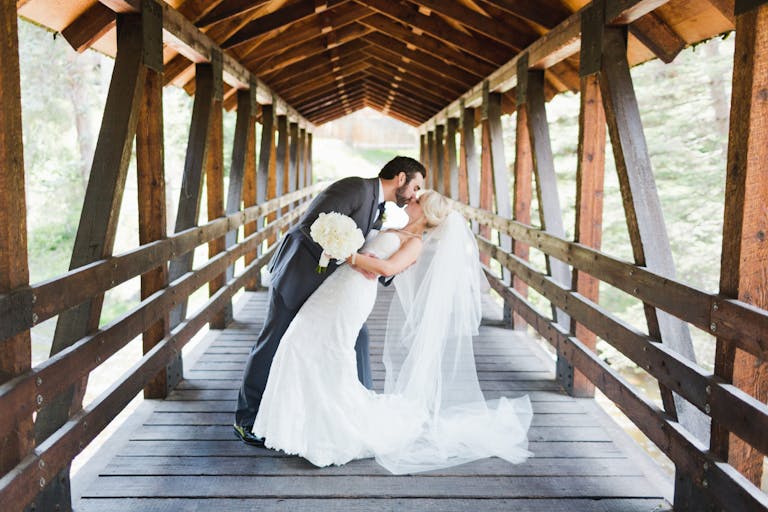 wedding at donovan pavillion in vail colorado with couple kissing on bridge | PartySlate