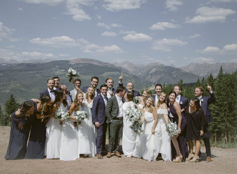 outdoor tented wedding at colorado mountain wedding venue with whole wedding party standing around bride and groom | PartySlate