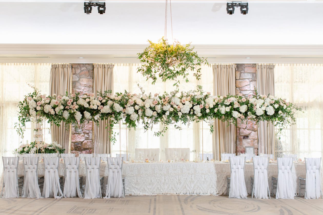Wedding with elevated greenery and white chairs covered in fringe | PartySlate