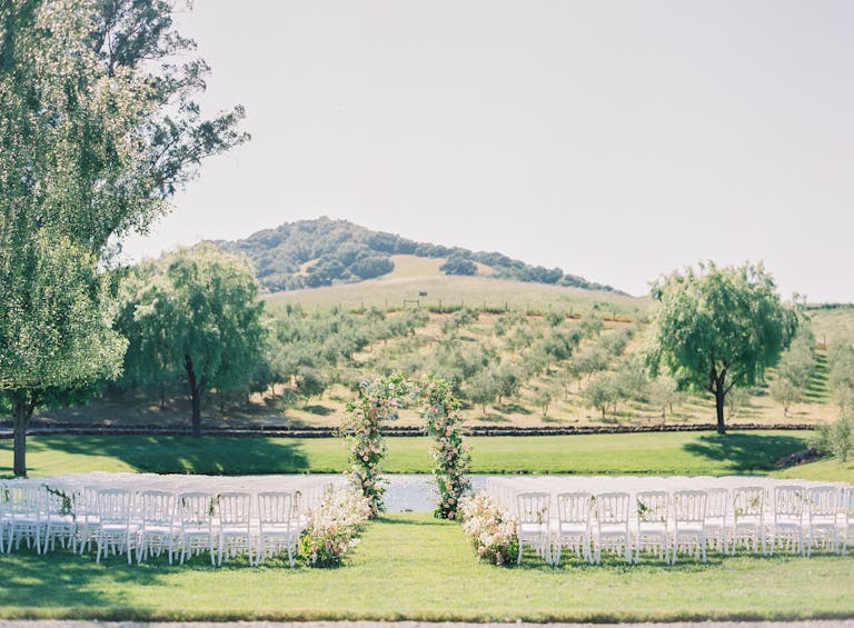 wedding aisle with pond and hills with vineyards behind and floral wedding arch | PartySlate
