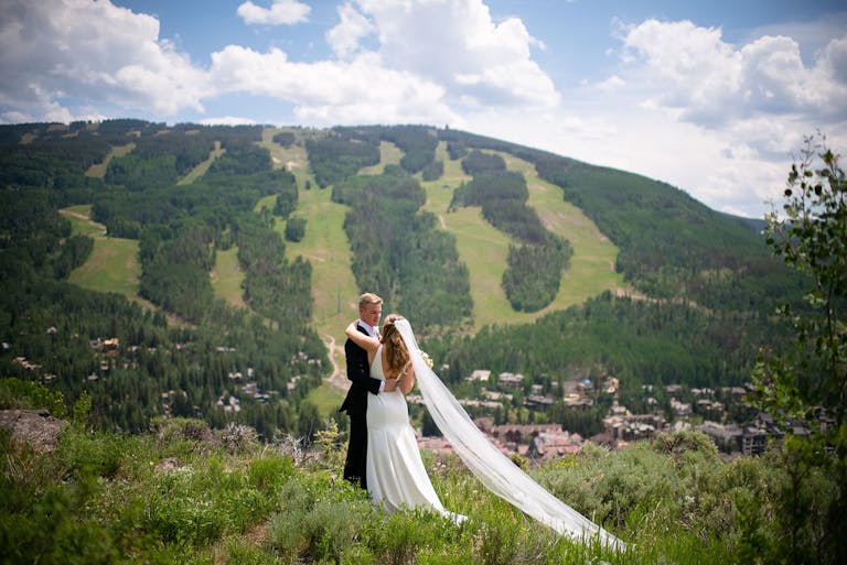 summer wedding couple standing outdoors in front of green mountain landscape | PartySlate