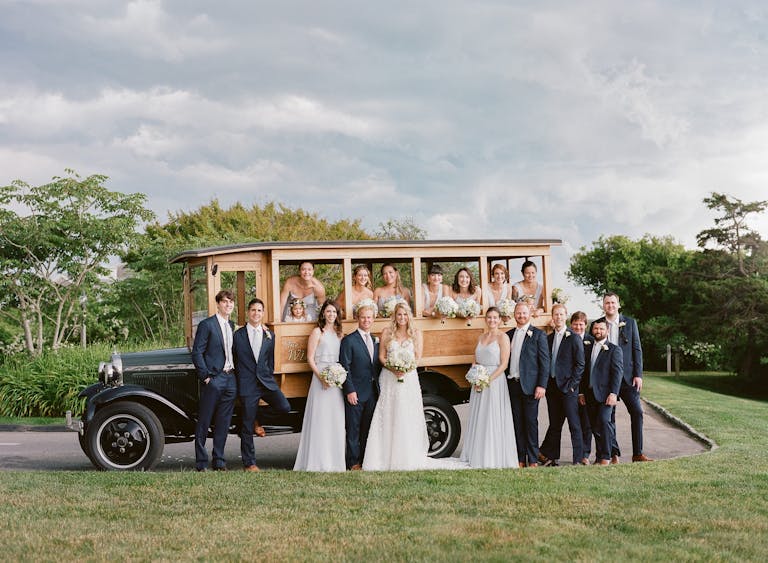 wedding in marthas vineyard with wedding party standing in front of an old car outside | PartySlate