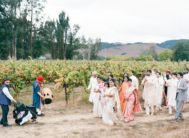 whimsical and romantic cultural wedding with couple's families walking through the vineyards | PartySlate