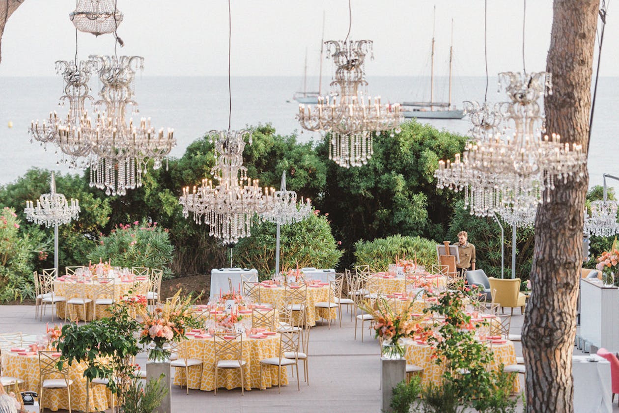 Outdoor Altbash party in the South of France with boats in the background and chandeliers hanging from trees | PartySlate