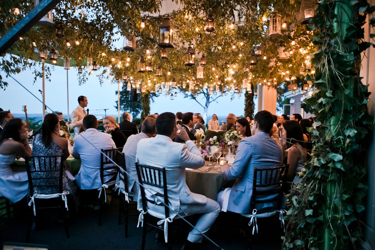 outdoor summer engagement party with guests seated under canopy trees with lights | PartySlate