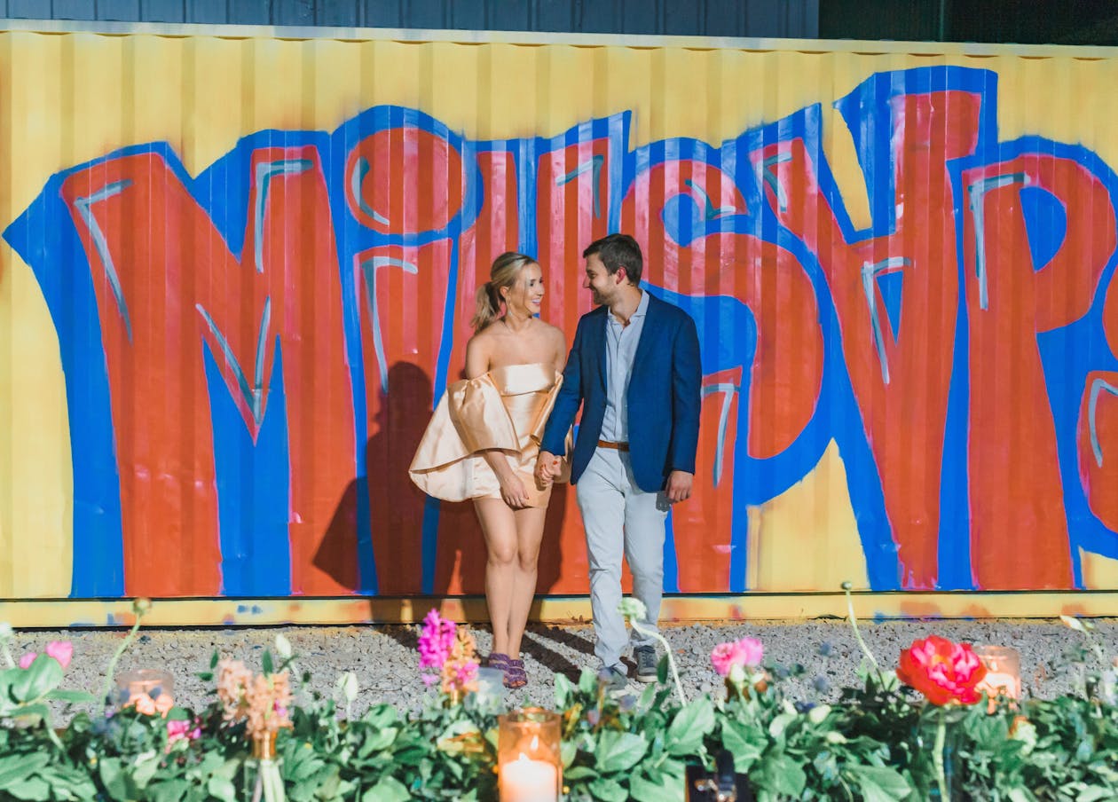 colorful spring engagement party couple standing in front of custom painted wall with their last name | PartySlate