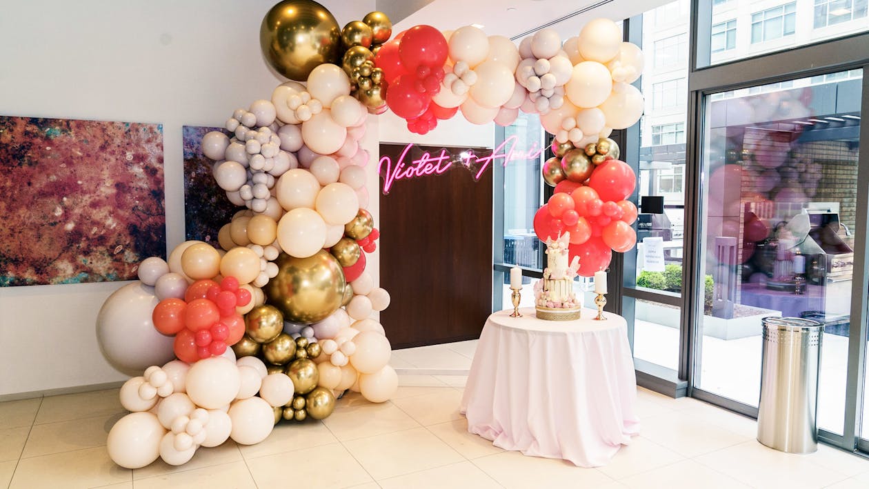 colorful engagement party with balloon arch by dessert table and neon sign on wall | PartySlate