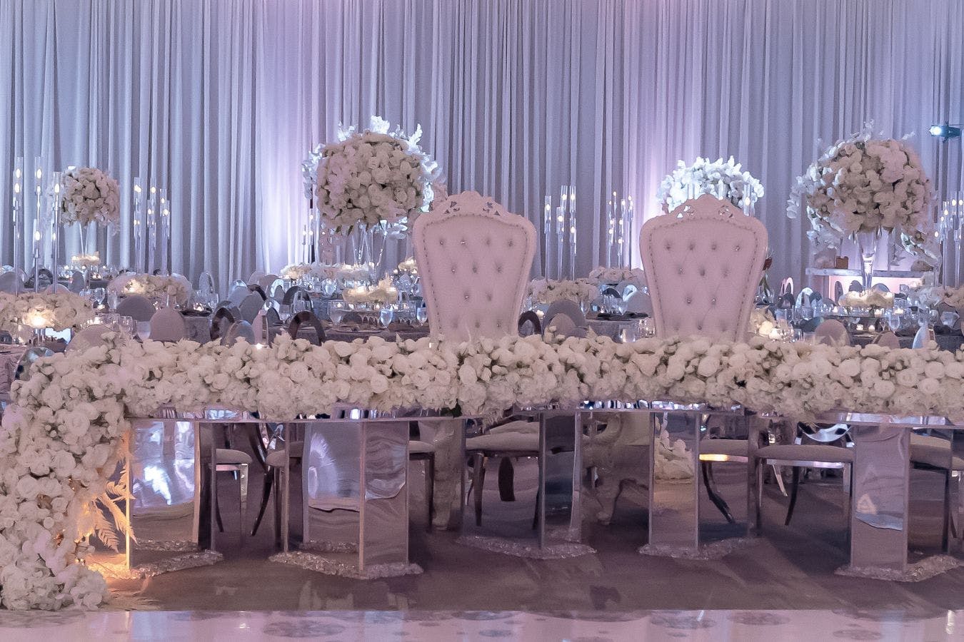 Glamorous mirrored sweetheart table with white throne seating and cascade of white table florals | PartySlate